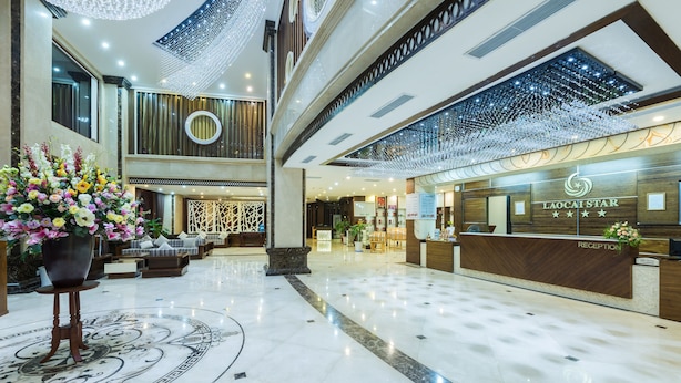 A spacious lobby with a reception desk, a large floral arrangement, and a modern chandelier.