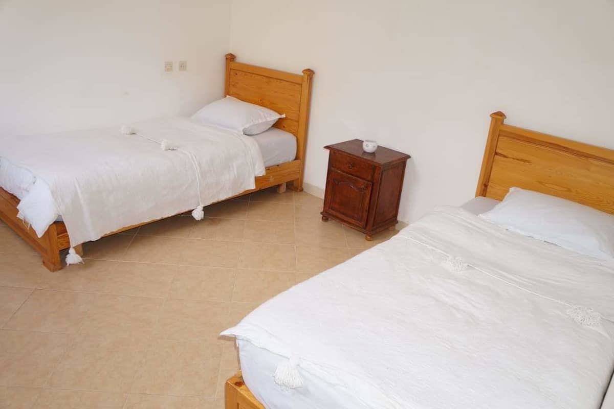 Two single beds with wooden headboards, a small wooden nightstand, and a tiled floor.