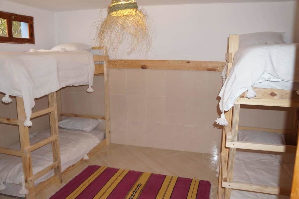A room with two bunk beds, a wooden headboard, a striped rug, and a hanging light fixture.