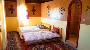 A bedroom with a wooden bed, patterned rug, and decorative wall art. - Hotel Boutaghrar (Ighil N'Oumgoun)