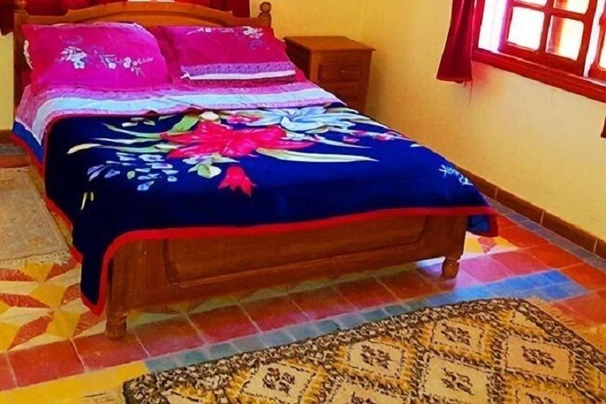 Ein Bett mit floralem Überwurf, einem Holzkopfende und roten Vorhängen.