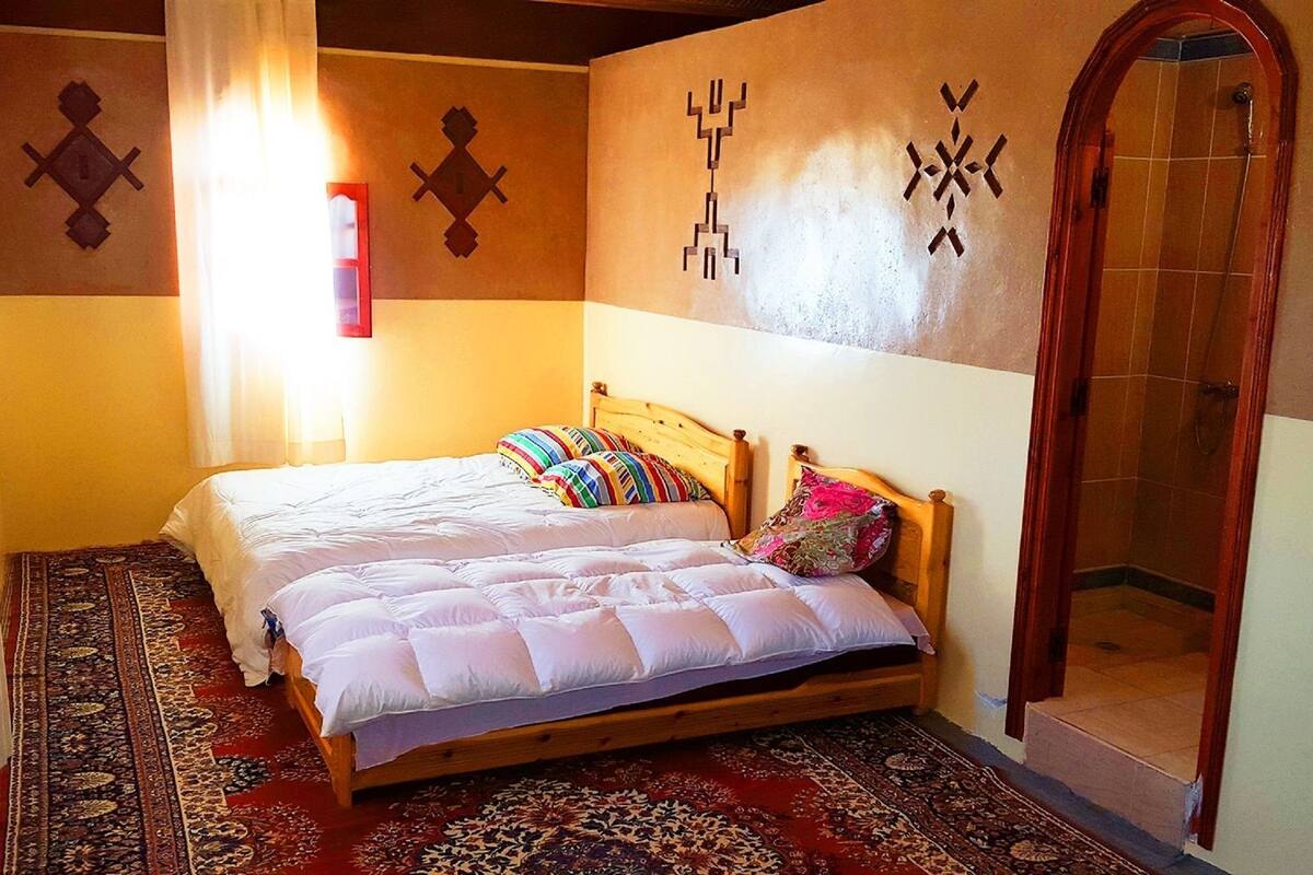 Ein Schlafzimmer mit einem hölzernen Bett, einem gemusterten Teppich und einer Duschkabine.