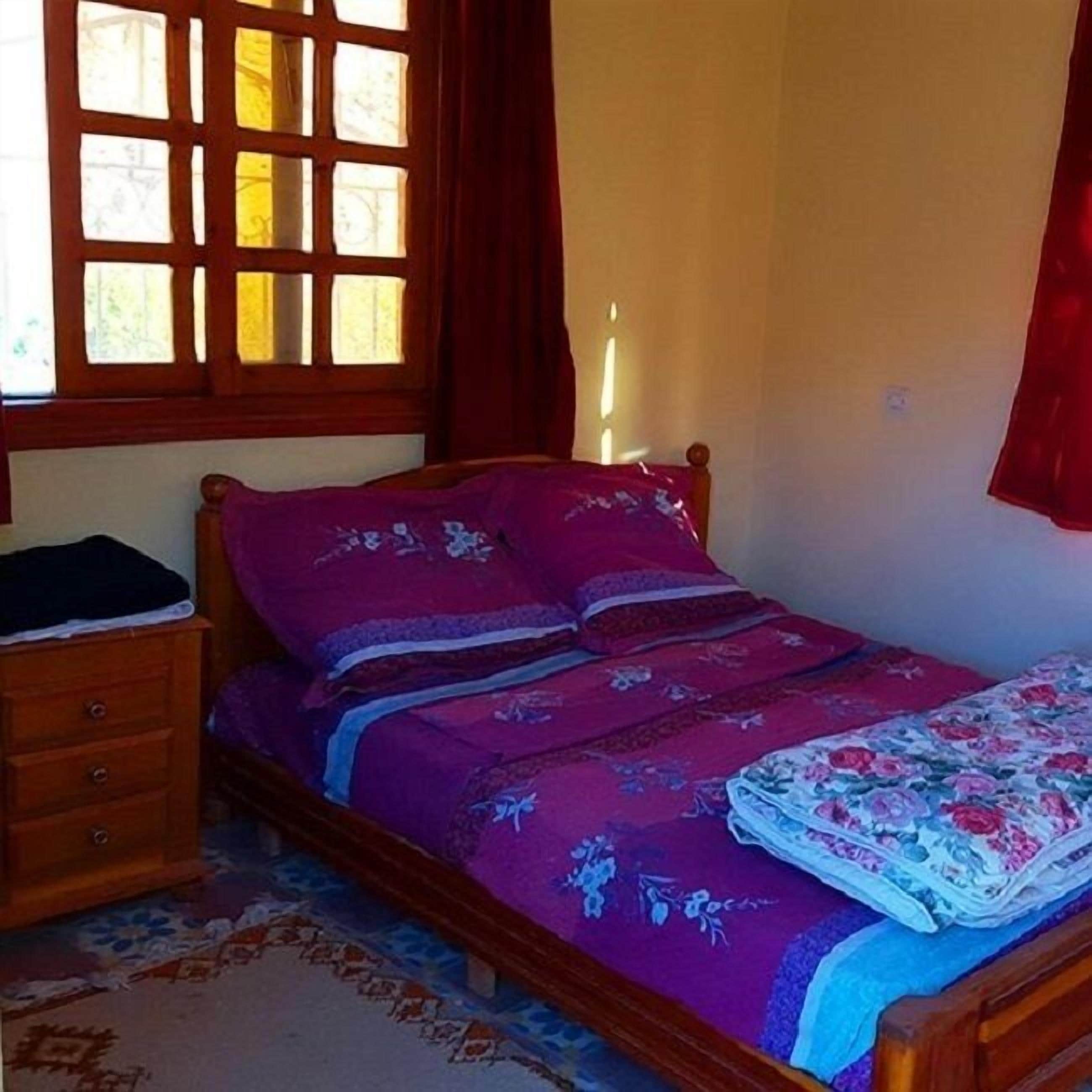 Un dormitorio con una cama de madera, una mesita de noche, un aparador y una ventana con cortinas.