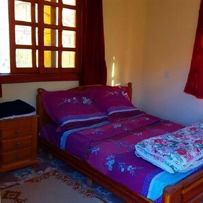 Een slaapkamer met een houten bed, een nachtkastje, een dressoir en een raam met gordijnen.