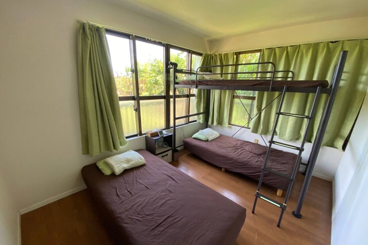 A dormitory room with bunk beds, a desk, and a window with curtains.