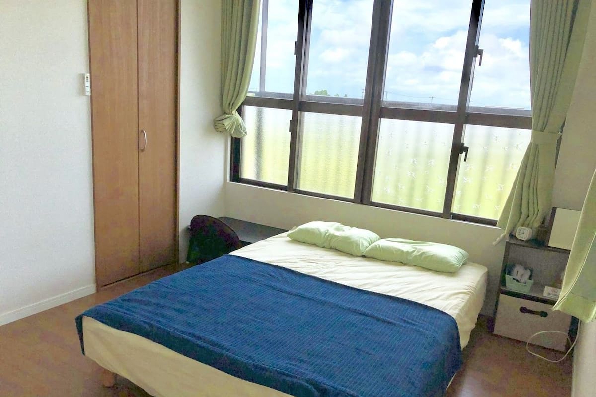A bedroom with a bed, a nightstand, a wardrobe, and a window with curtains.