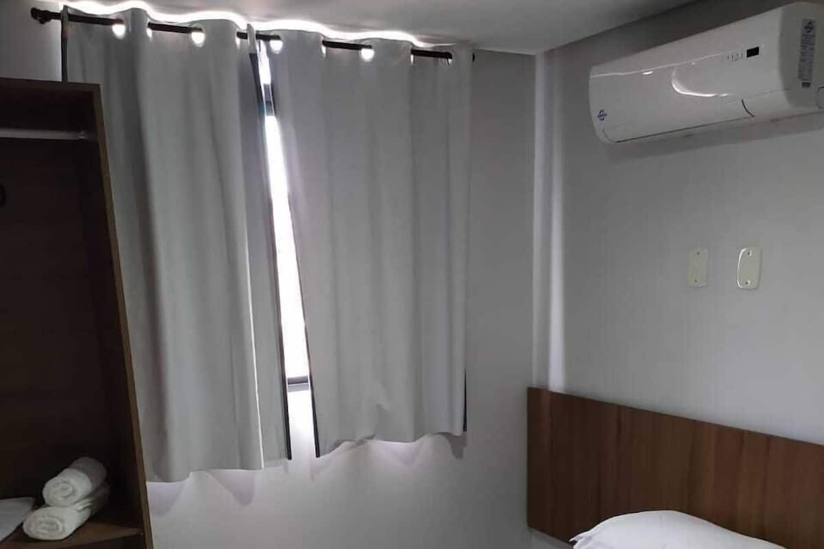 A single bed with white bedding, a wooden headboard, a wardrobe, and an air conditioning unit on the wall.