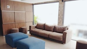 A modern living room with a beige sofa, two blue ottomans, and a wooden cabinet with a Wi-Fi symbol. - Hotel Campina Executivo (Campina Grande)