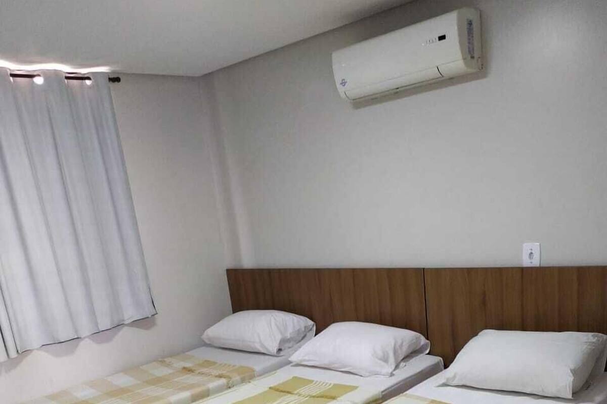 A hotel room with two single beds, a wooden headboard, an air conditioning unit, and a window with curtains.