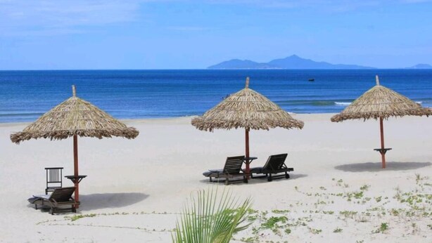 A beach with three thatched umbrellas and lounge chairs. - Motel Thanh Long (Da Nang)