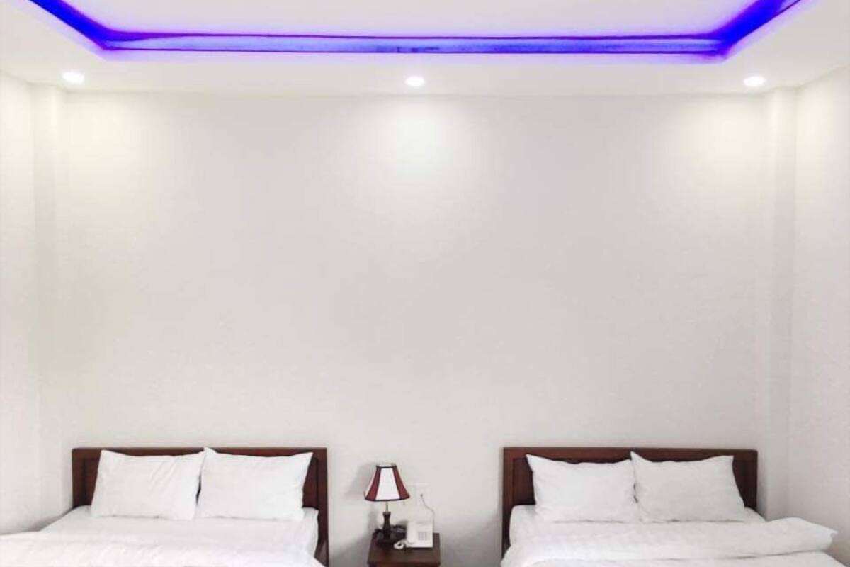 A hotel room with two beds, white bedding, a nightstand with a lamp, and blue LED lighting on the ceiling.