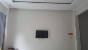 A room with a flat-screen TV mounted on the wall, a door on the right, and a window with blinds on the left. - Motel Thanh Long (Da Nang)