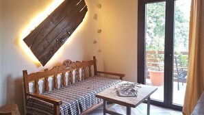 A wooden bench with a patterned cushion, a table with a decorative item, and a view of an outdoor area with potted plants through a glass door. - Victoria's Country Apartments (Zagora-Mouresi)