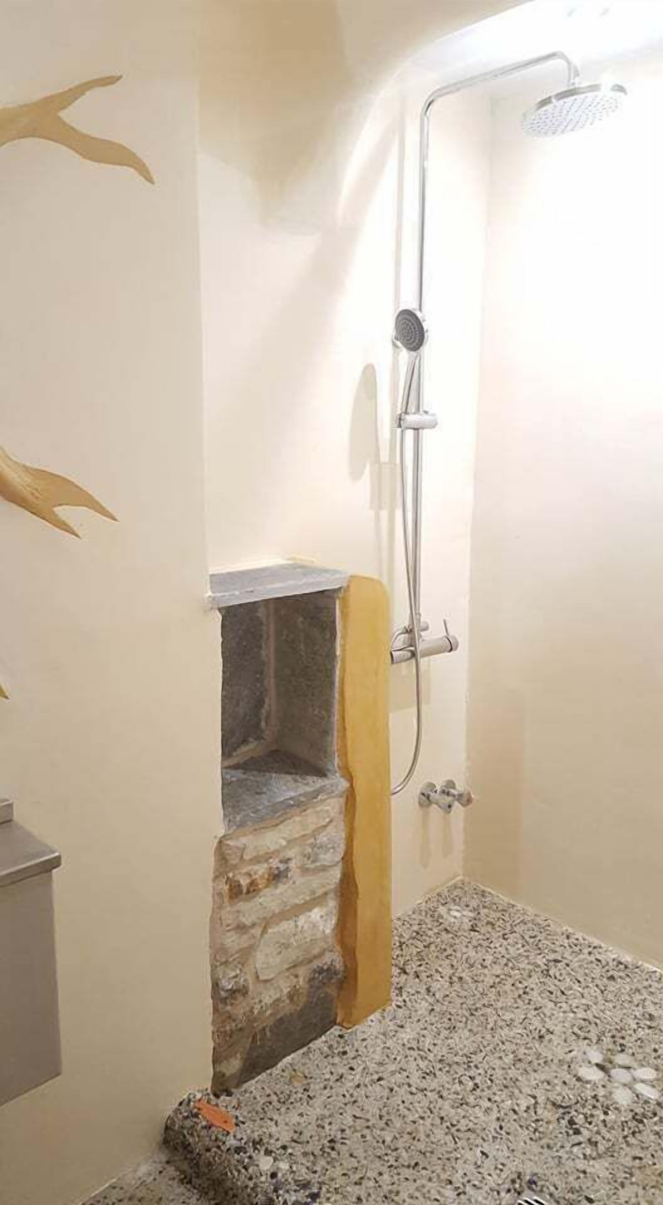 A bathroom with a shower, a stone wall, and a small sink area.