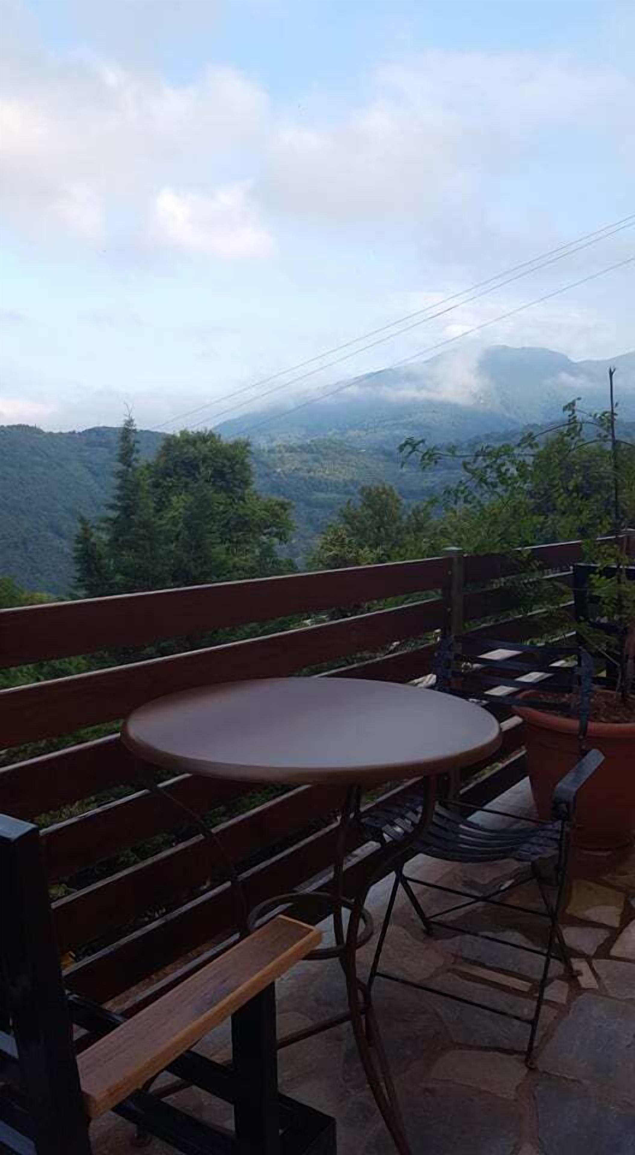 Une terrasse avec un banc en bois et une petite table ronde, d’où l’on peut admirer un paysage montagneux.