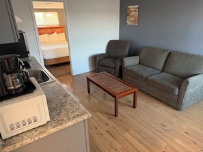 A modern living room with a sofa, a coffee table, and a kitchen area with a coffee maker. - Out West Motel (Milton-Freewater)