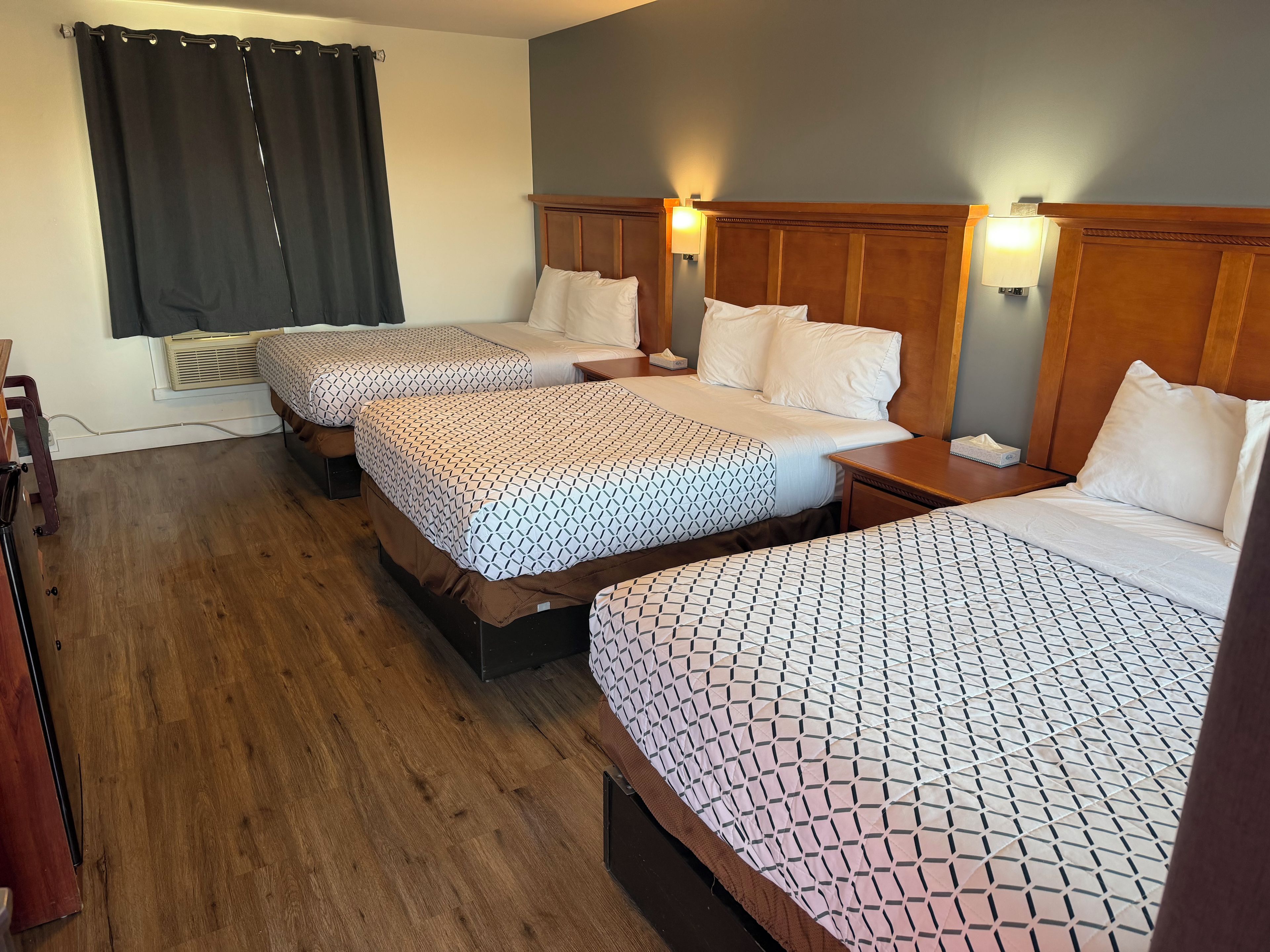 Une chambre d’hôtel avec trois lits, des têtes de lit en bois et des lampes de chevet.