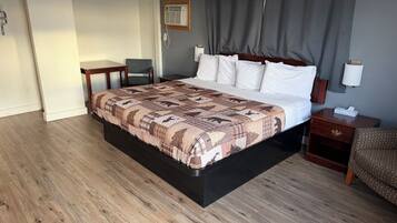 A hotel room with a large bed, a bedside table, a chair, a desk, and a wall-mounted air conditioner.