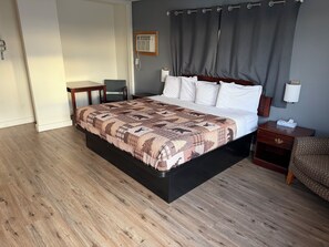 A hotel room with a large bed, a bedside table, a chair, a desk, and a wall-mounted air conditioner. - Out West Motel (Milton-Freewater)