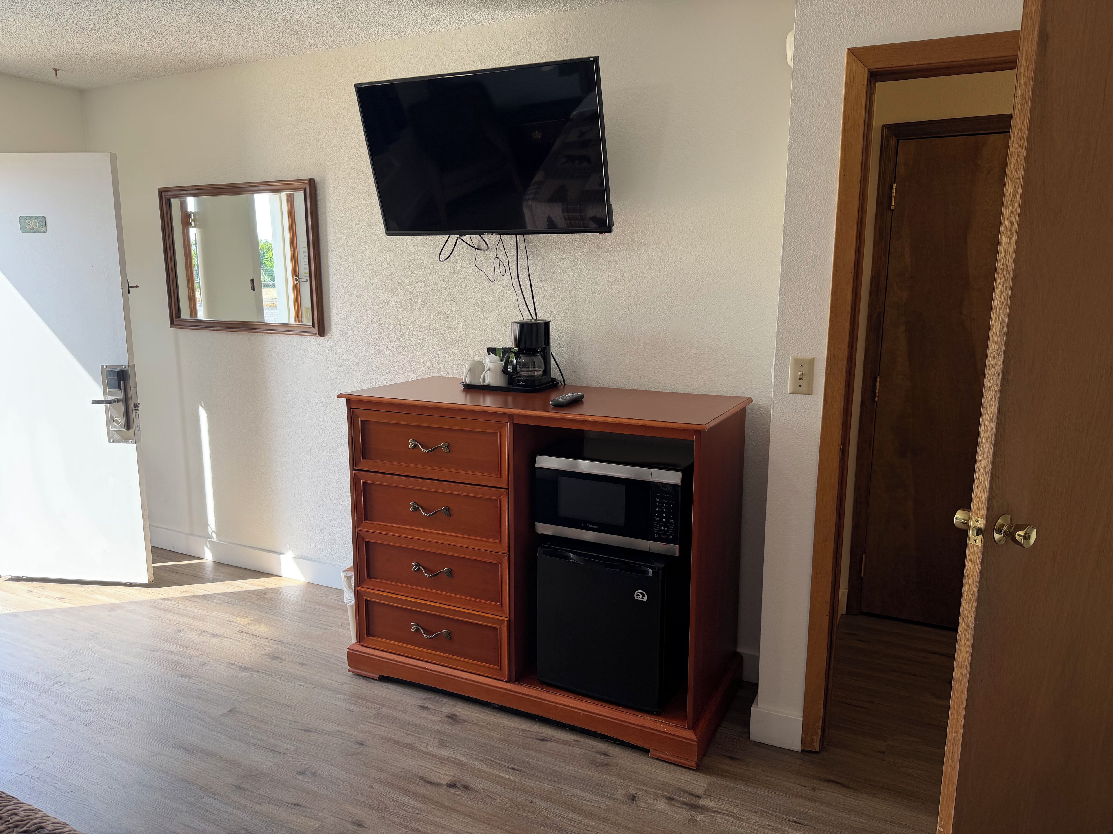Een kamer met een houten kast, een aan de muur bevestigde televisie, een magnetron en een koelkast.