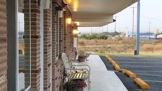 Un área de estar al aire libre con bancos y una jardinera con flores, contigua a un edificio de paredes de ladrillo y ventanas amplias.