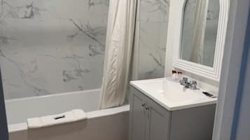 Un baño con bañera, lavabo, inodoro y espejo con iluminación.