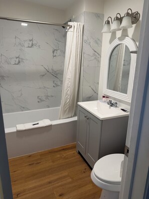 A bathroom with a bathtub, a sink, a toilet, and a mirror with lights. - Out West Motel (Milton-Freewater)