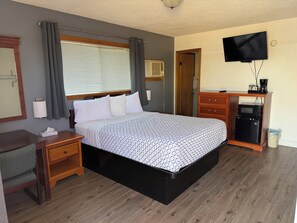 A hotel room with a bed, bedside table, lamp, TV, and a small kitchenette.
