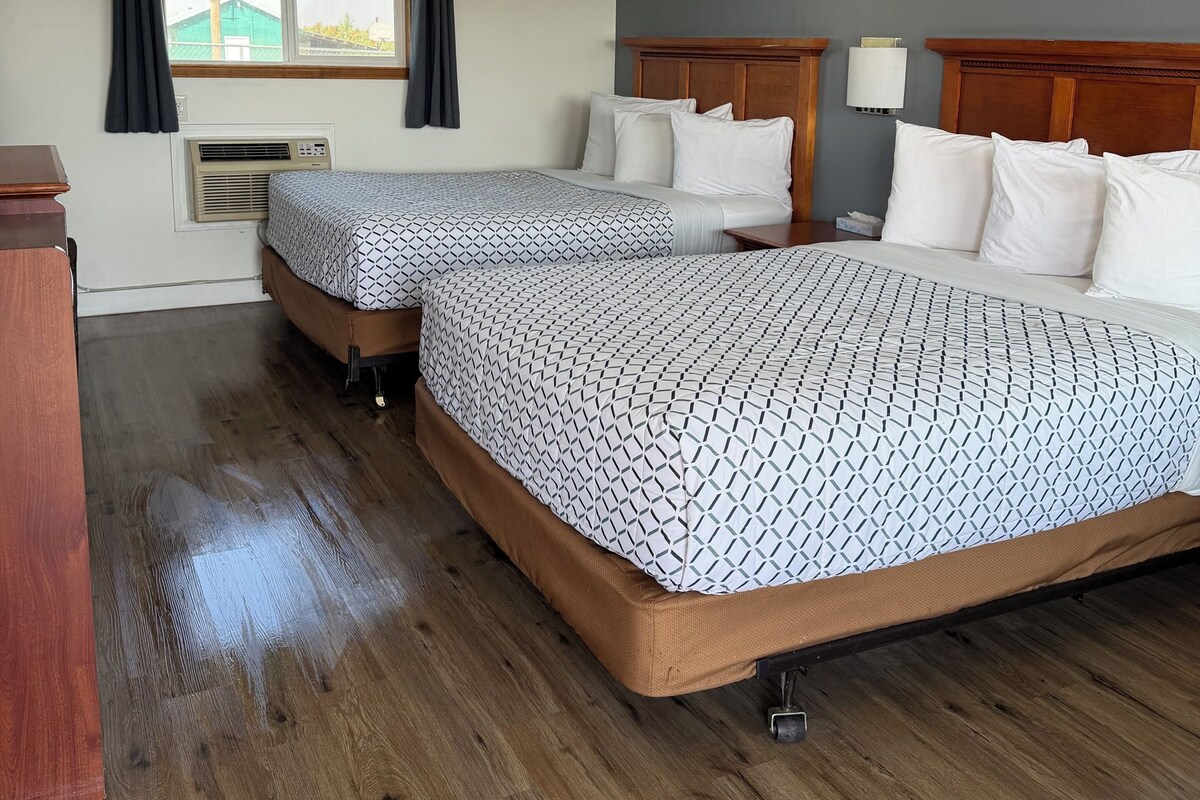 Habitación de hotel con dos camas, una ventana con cortinas, un cabecero de madera y una lámpara en el techo.