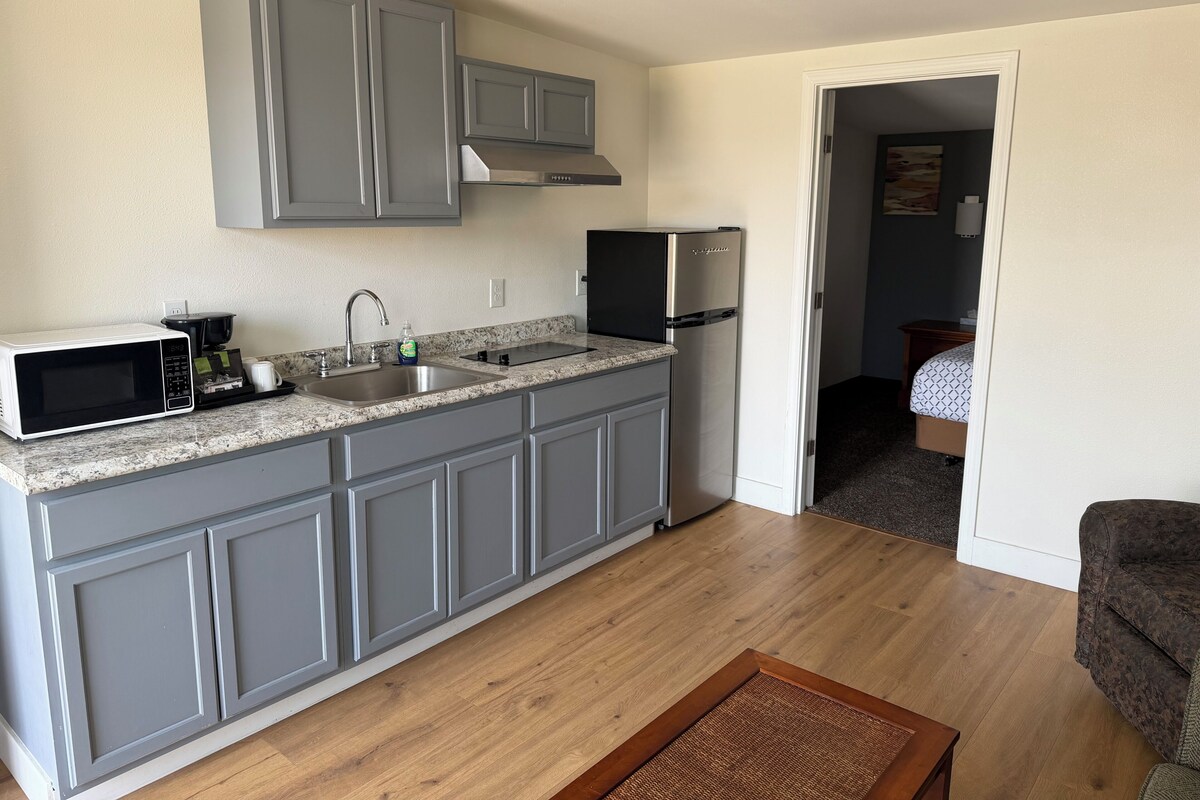 A compact kitchen with grey cabinets, a stainless steel refrigerator, a microwave, and a coffee maker.