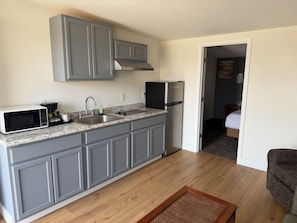 A compact kitchen with grey cabinets, a stainless steel refrigerator, a microwave, and a coffee maker. - Out West Motel (Milton-Freewater)