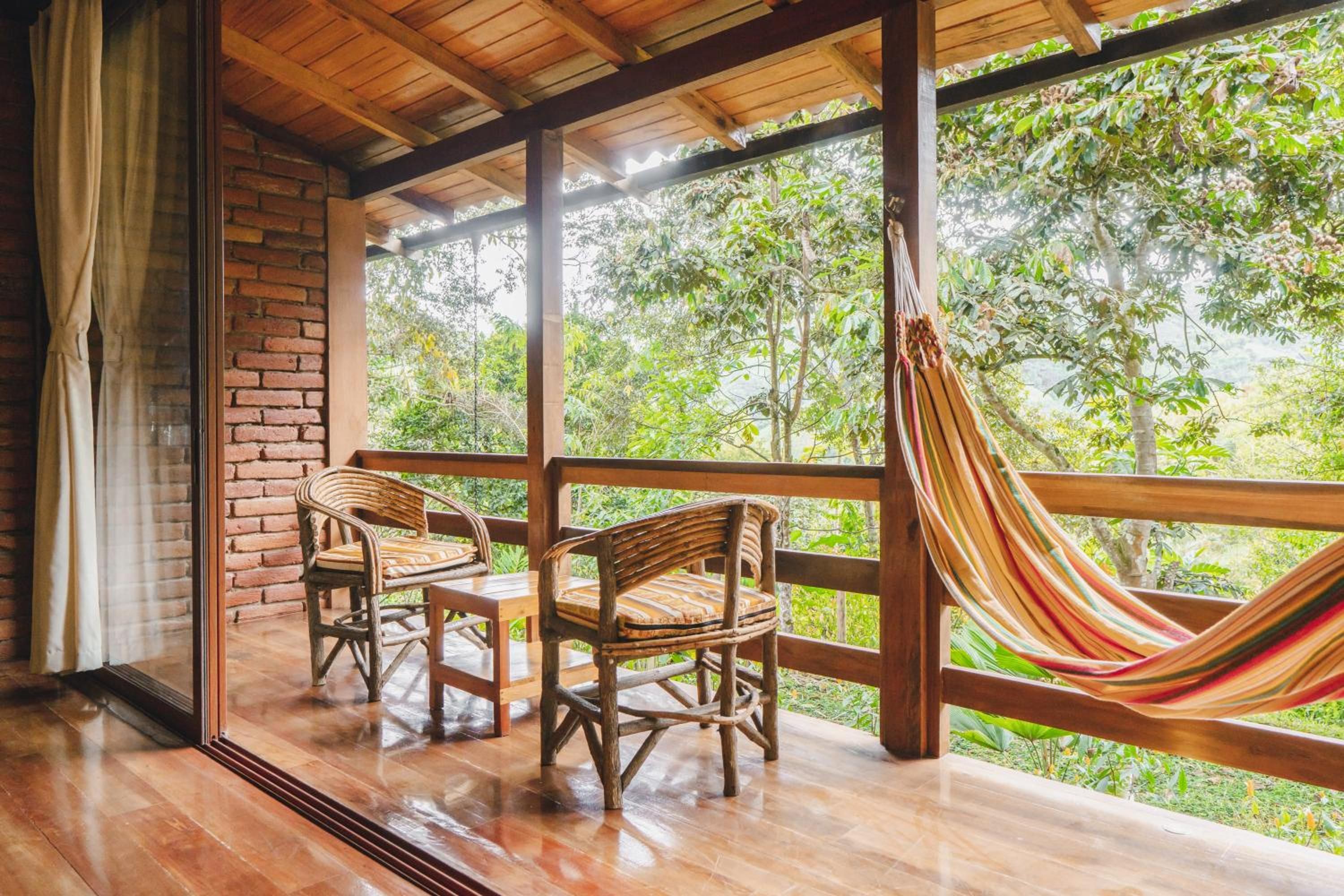A wooden room with a large window, two wicker chairs, and a hammock.