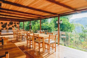 An outdoor wooden deck with tables and chairs, surrounded by lush greenery and a mountainous backdrop. - Piripe Wellness Lodge (Pacto)