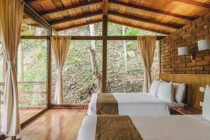 Una habitación con dos camas, techo de madera, ventanas grandes con cortinas y una pared de ladrillo.