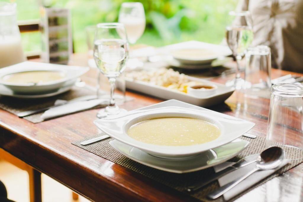 A dining table set with plates of soup, glasses of water, and cutlery.
