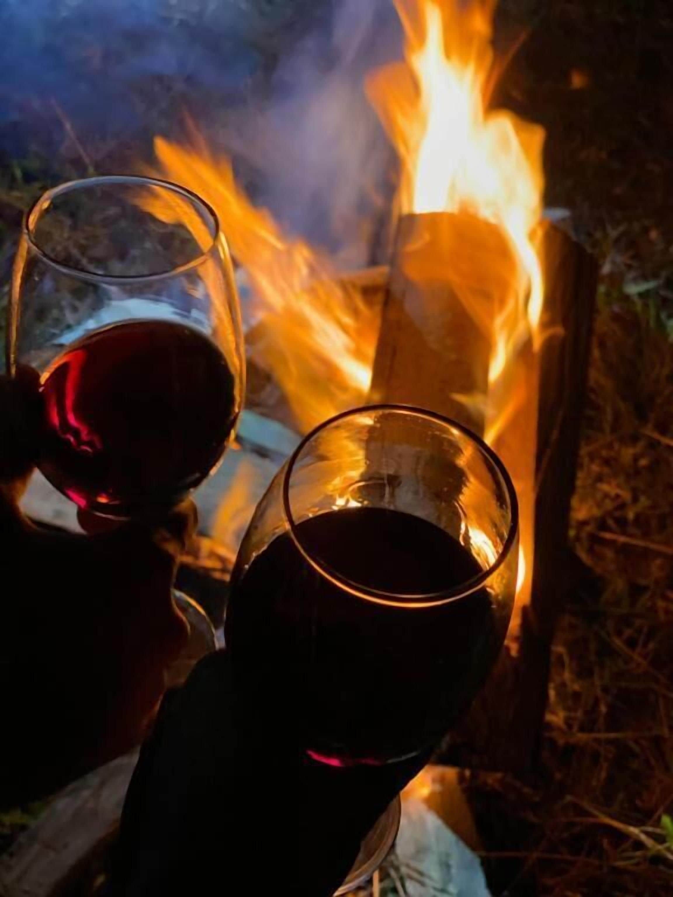 Dos copas de vino tinto cerca de una fogata.