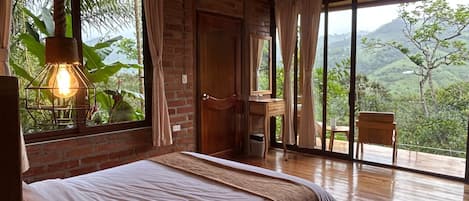 Un dormitorio con cama, techo de madera, ventanas amplias y vista a zonas verdes.