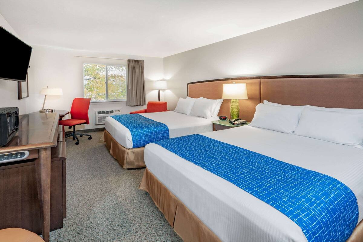 A hotel room with two beds, a desk, a chair, and a TV.