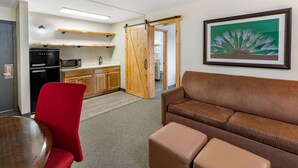 Un espacio habitable compacto con kitchenette, una silla roja, un sofá marrón y una obra de arte enmarcada en la pared.