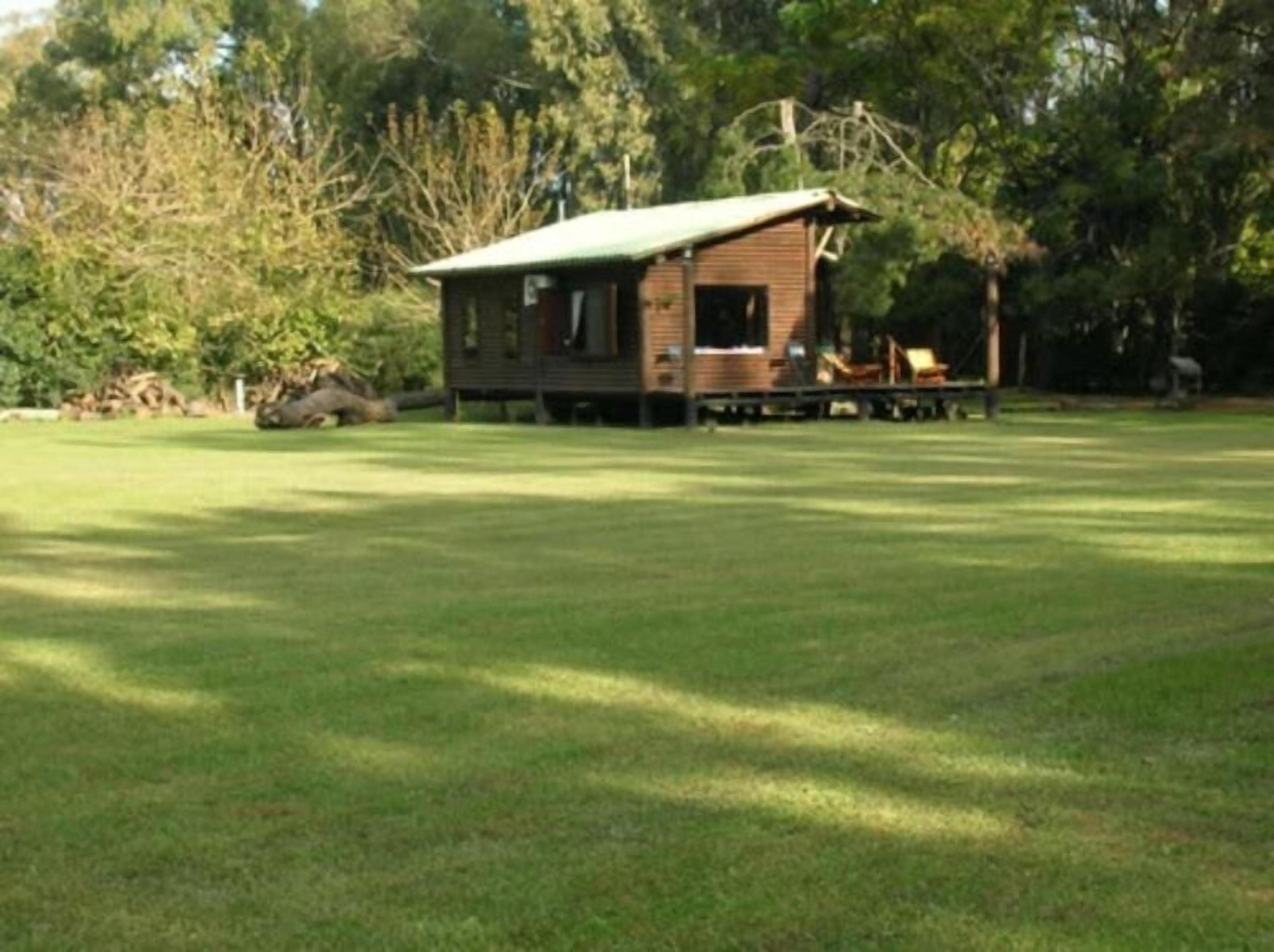 Une petite cabane en bois, surmontée d’un toit vert, entourée d’un champ herbeux et d’arbres.