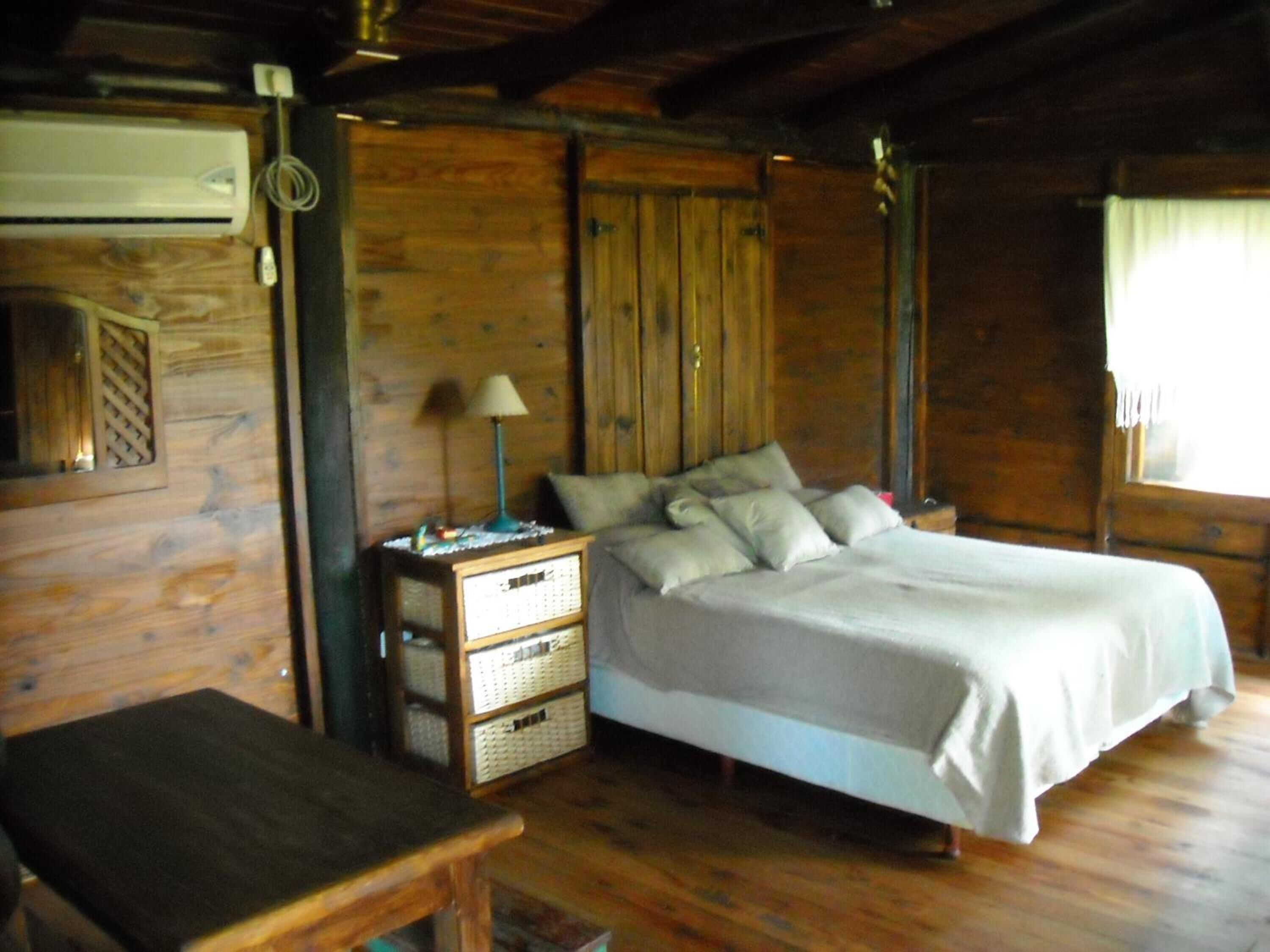 A wooden cabin bedroom with a bed, bedside table, lamp, and a small desk.