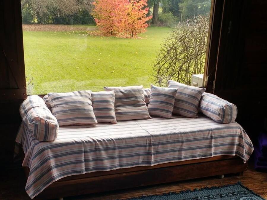 Una habitación acogedora con una cama de madera tipo banco, un ventanal grande y un tapete azul con estampado floral detallado.