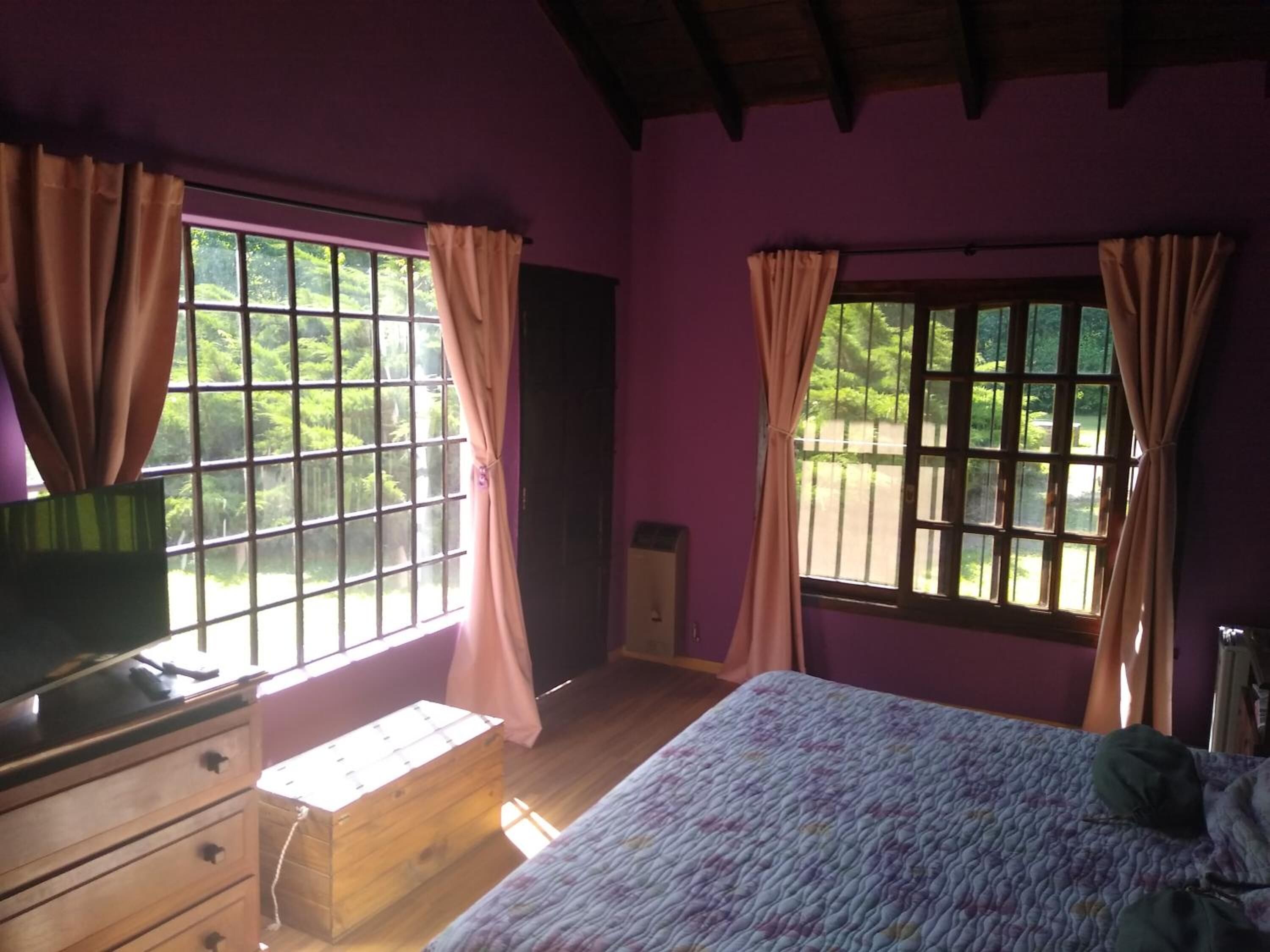 Ein Schlafzimmer mit einem Bett, einer Holzkommode und zwei mit Vorhängen versehenen Fenstern.