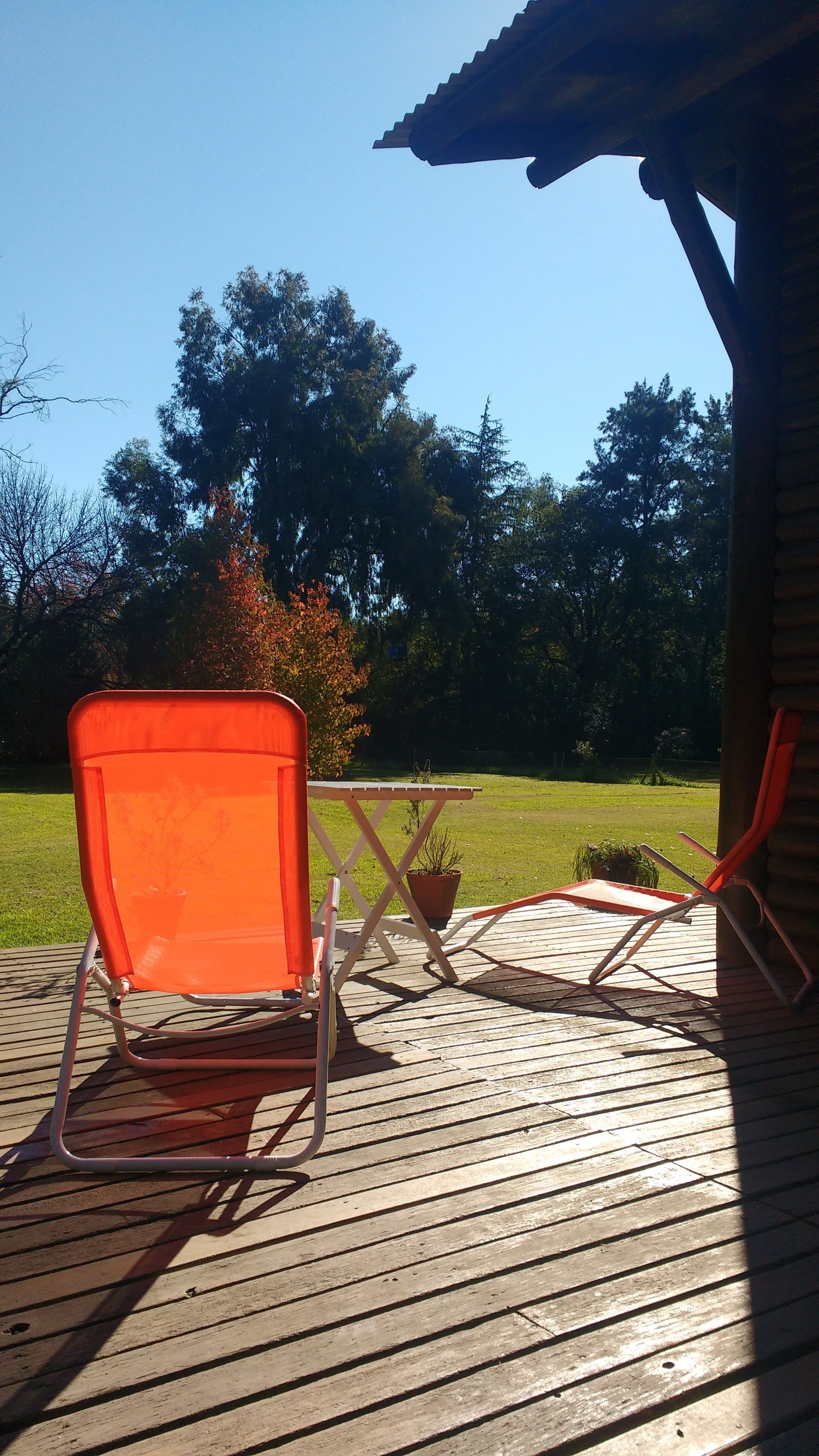 An outdoor patio with a wooden deck, a metal table, and two orange chairs.