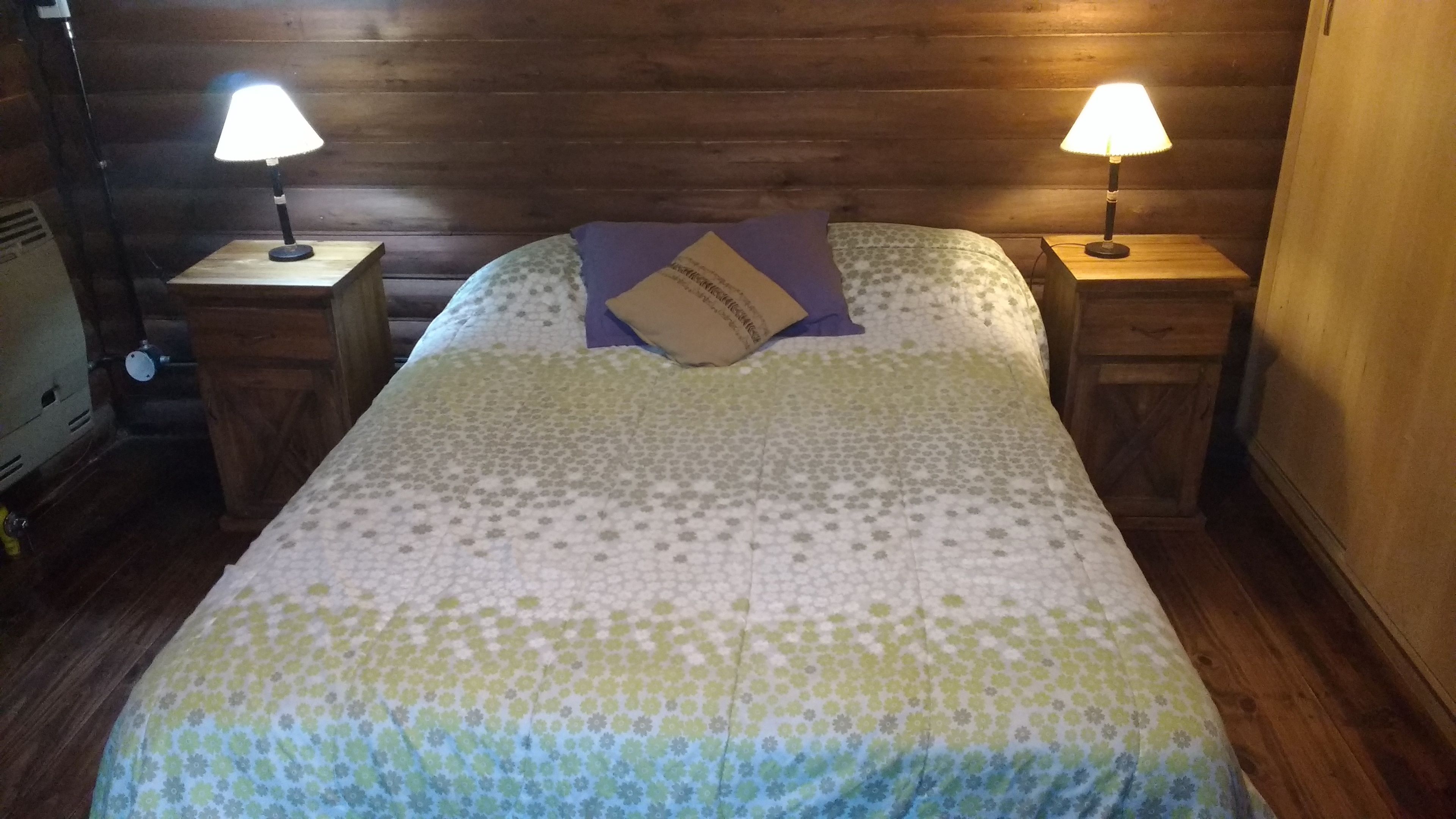 A bed with a floral-patterned bedspread, two bedside lamps, and a wooden headboard.