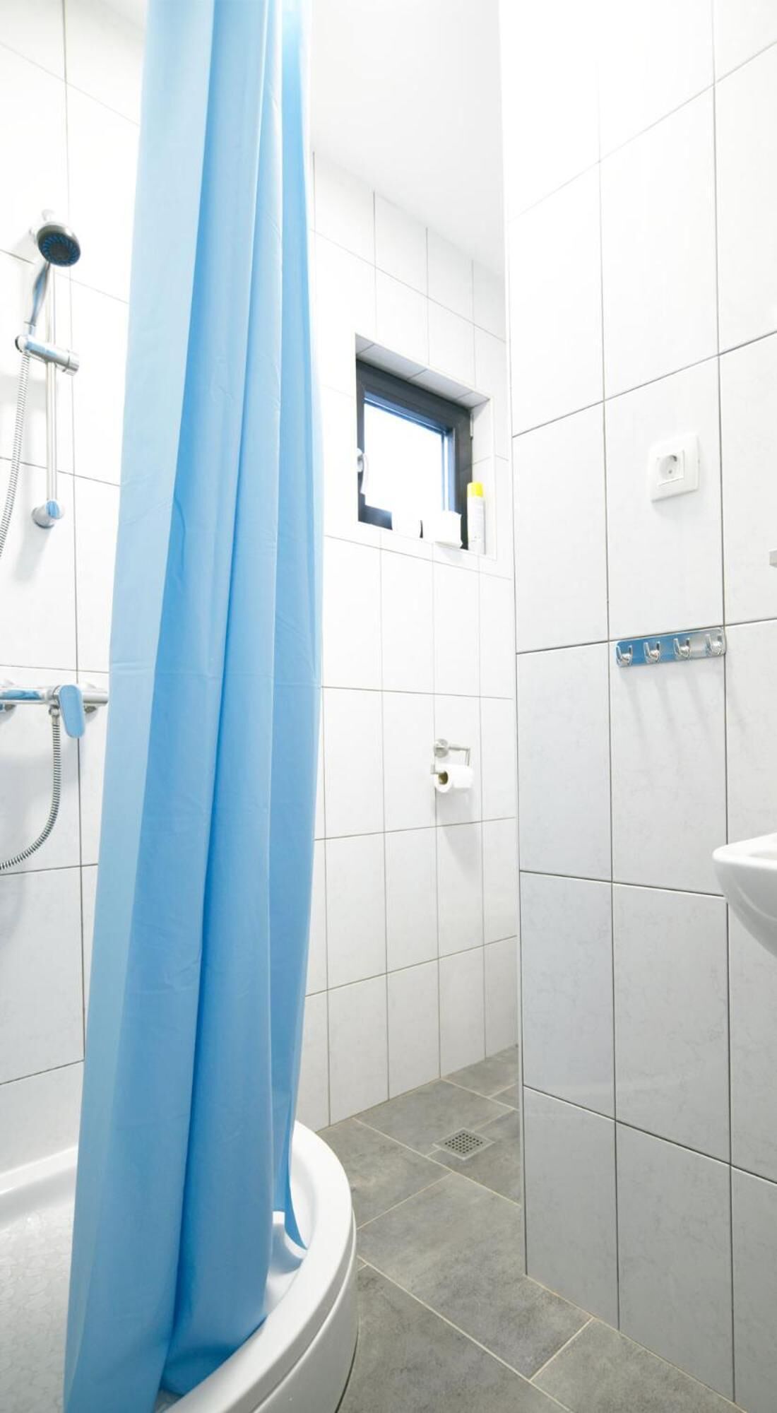 Ein Badezimmer mit Duschvorhang, Fenster, Waschbecken und Handtuchhalter.
