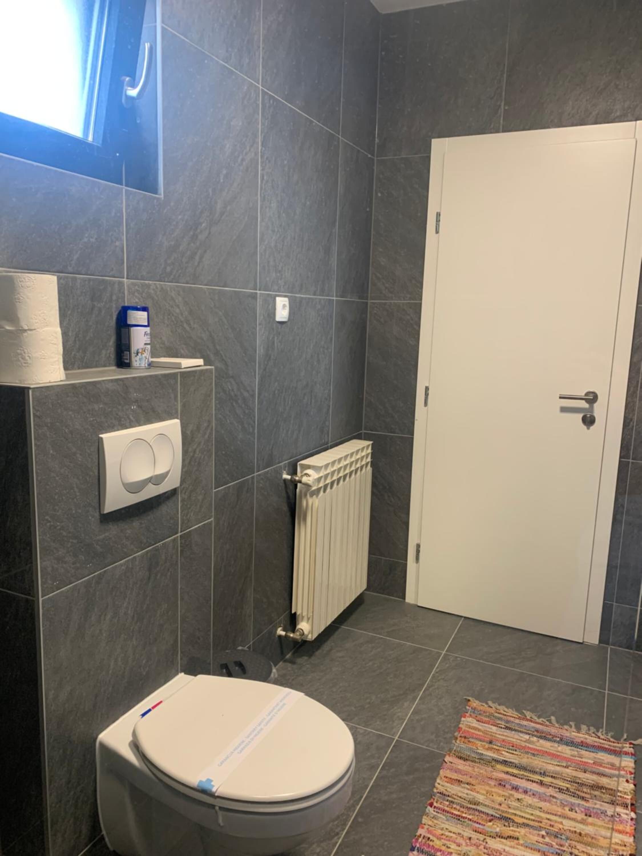 A bathroom with a toilet, a radiator, a towel dispenser, and a door.