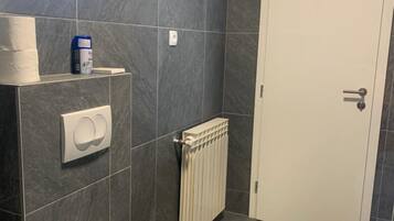 A bathroom with a toilet, a radiator, a towel dispenser, and a door.