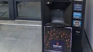A coffee vending machine with a sign advising to wash hands before using.