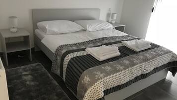 A neatly made bed with white linens, a grey headboard, and a patterned throw blanket.